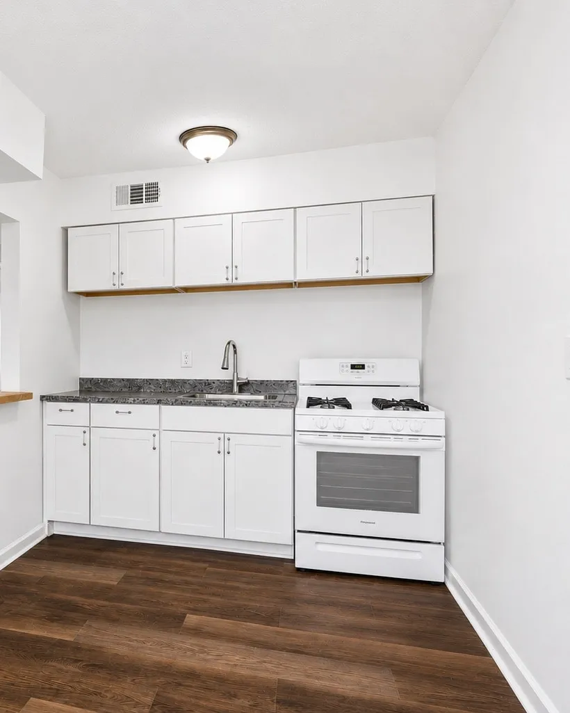 Renovated kitchen with white shaker cabinets, a granite counter, a gas range, and dark wood-look plank flooring in a Three Roses rental